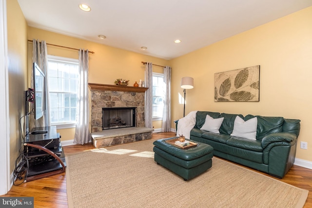 living room featuring hardwood / wood-style floors, a stone fireplace, and a healthy amount of sunlight