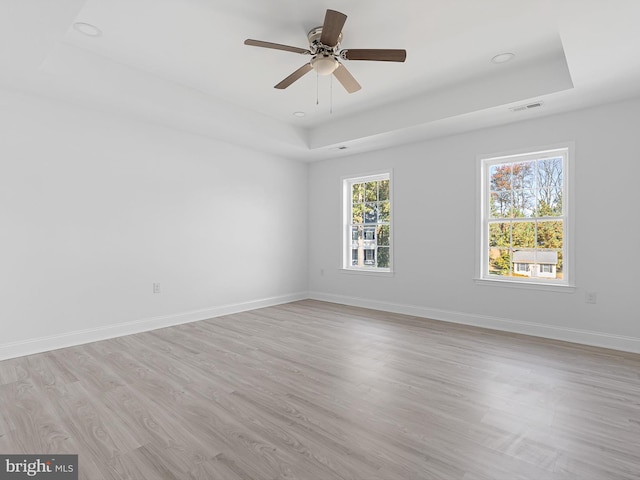 empty room with light hardwood / wood-style floors, a raised ceiling, and ceiling fan