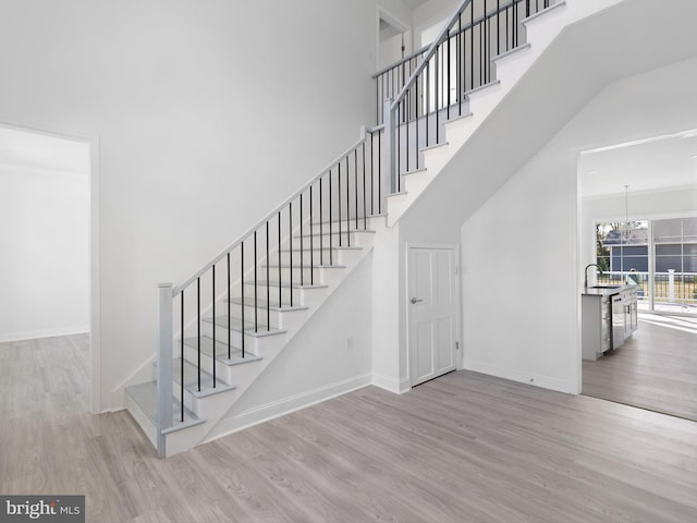 stairway featuring a notable chandelier, wood-type flooring, and a high ceiling