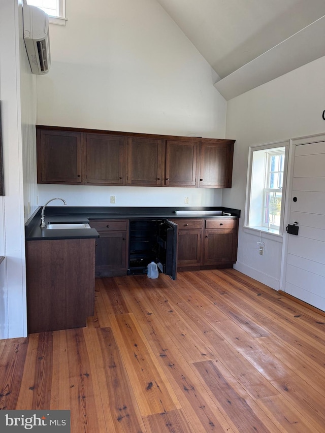 kitchen with sink, light hardwood / wood-style flooring, dark brown cabinetry, and high vaulted ceiling