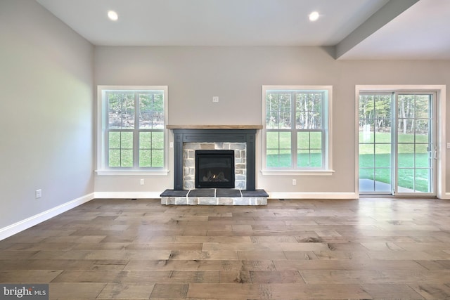 unfurnished living room featuring a healthy amount of sunlight, wood-type flooring, and a stone fireplace