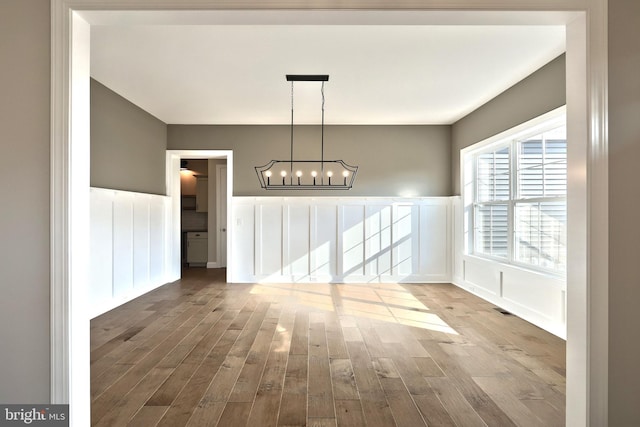 unfurnished dining area featuring a chandelier and wood-type flooring