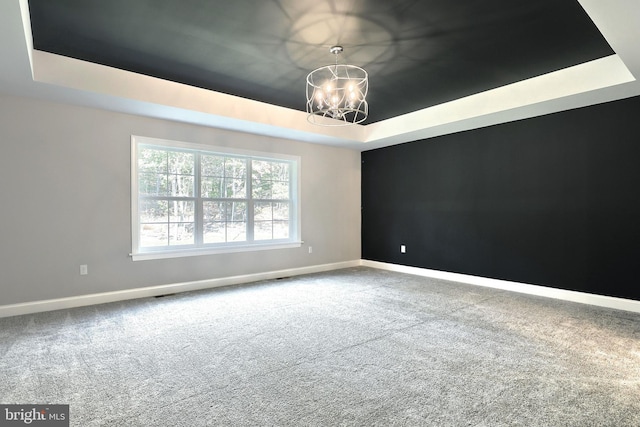 carpeted spare room with a notable chandelier and a tray ceiling