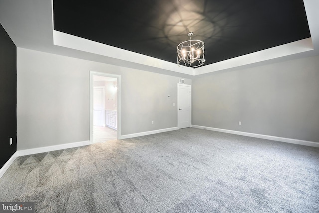 spare room with carpet flooring, an inviting chandelier, and a raised ceiling