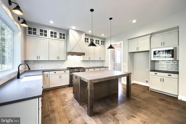 kitchen featuring custom exhaust hood, stainless steel appliances, dark wood-type flooring, pendant lighting, and a center island