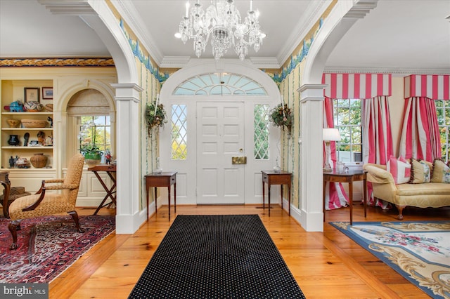 foyer featuring decorative columns, crown molding, wood-type flooring, and an inviting chandelier