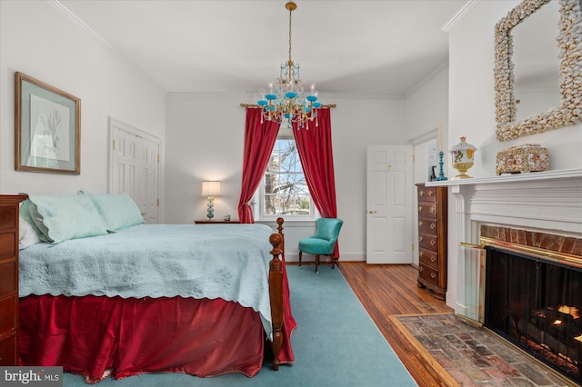 bedroom with hardwood / wood-style flooring, ornamental molding, a chandelier, and a brick fireplace