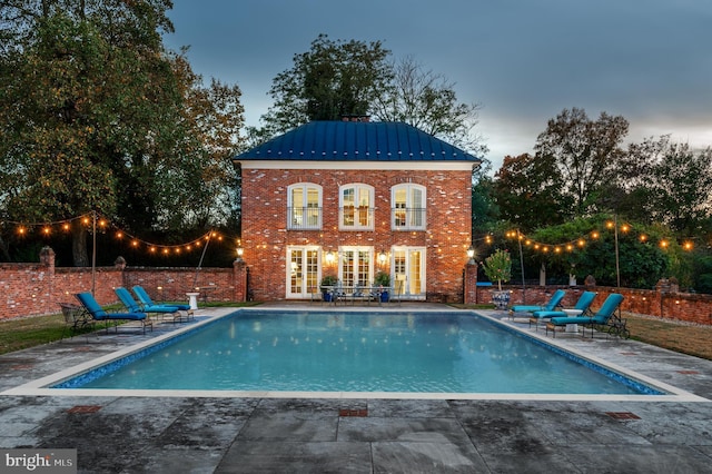 pool at dusk with french doors and a patio