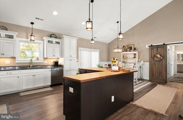 kitchen featuring wooden counters, a center island, a barn door, decorative light fixtures, and white cabinetry