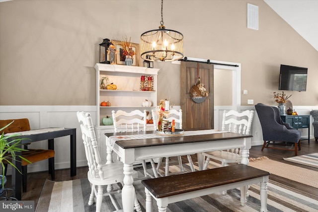 dining room featuring hardwood / wood-style floors, a barn door, a notable chandelier, and high vaulted ceiling