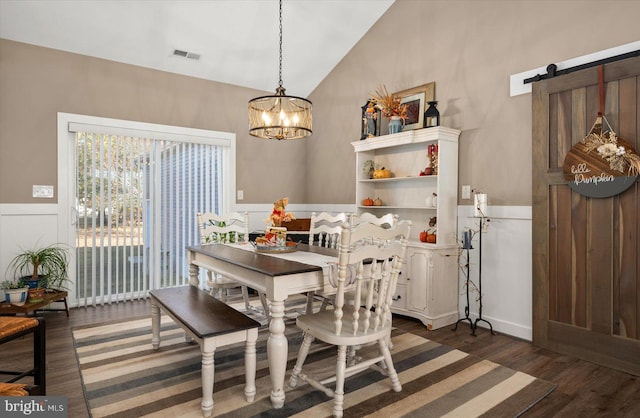 dining room featuring lofted ceiling, dark hardwood / wood-style floors, a barn door, and a chandelier