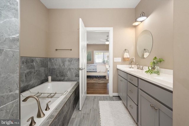 bathroom with vanity, a relaxing tiled tub, hardwood / wood-style flooring, and ceiling fan