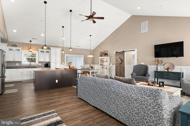 living room with ceiling fan, a barn door, high vaulted ceiling, dark hardwood / wood-style floors, and sink