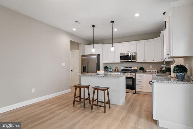 kitchen with hanging light fixtures, light hardwood / wood-style flooring, appliances with stainless steel finishes, a kitchen island, and white cabinetry