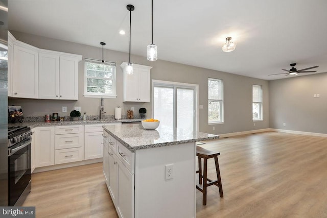 kitchen featuring a kitchen island, pendant lighting, light hardwood / wood-style flooring, stainless steel range oven, and white cabinetry