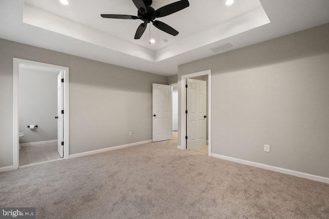 unfurnished bedroom with light carpet, ensuite bathroom, ceiling fan, and a tray ceiling