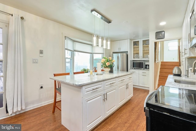 kitchen with appliances with stainless steel finishes, a kitchen island, sink, decorative light fixtures, and white cabinetry