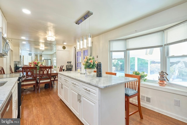 kitchen with white cabinets, decorative light fixtures, a kitchen island, and hardwood / wood-style floors