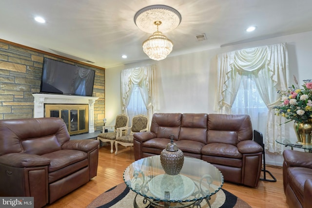 living room featuring a stone fireplace, a wealth of natural light, light hardwood / wood-style flooring, and a chandelier