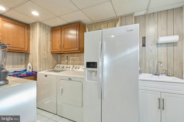 clothes washing area featuring wood walls, sink, light tile patterned floors, and independent washer and dryer