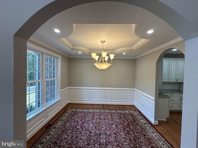 unfurnished dining area featuring crown molding, a tray ceiling, dark hardwood / wood-style flooring, and a chandelier