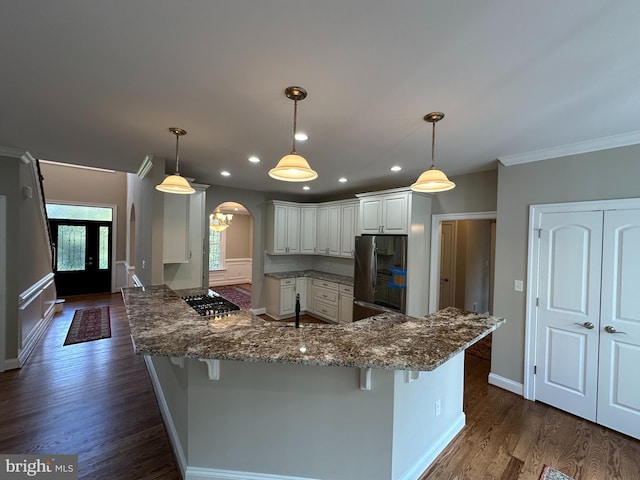 kitchen featuring kitchen peninsula, appliances with stainless steel finishes, a breakfast bar, dark wood-type flooring, and pendant lighting