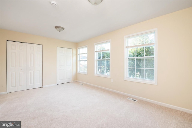 unfurnished bedroom with light carpet and two closets