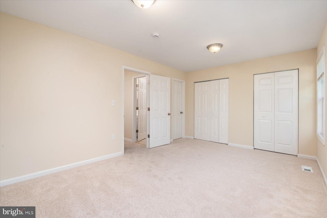 unfurnished bedroom featuring light carpet and multiple closets