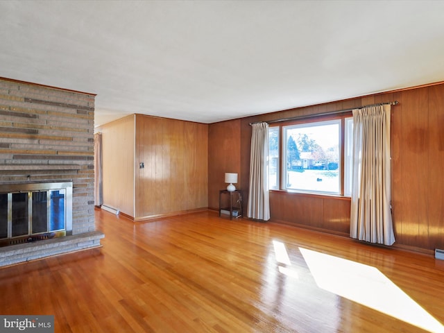 unfurnished living room featuring a fireplace, wood walls, and light wood-type flooring