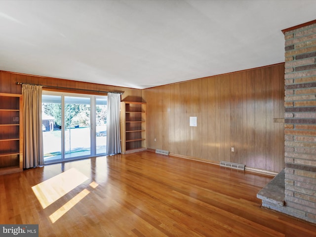 unfurnished living room with hardwood / wood-style flooring, a brick fireplace, and wooden walls