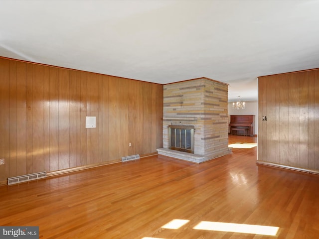 unfurnished living room with wood-type flooring, an inviting chandelier, wooden walls, and a fireplace