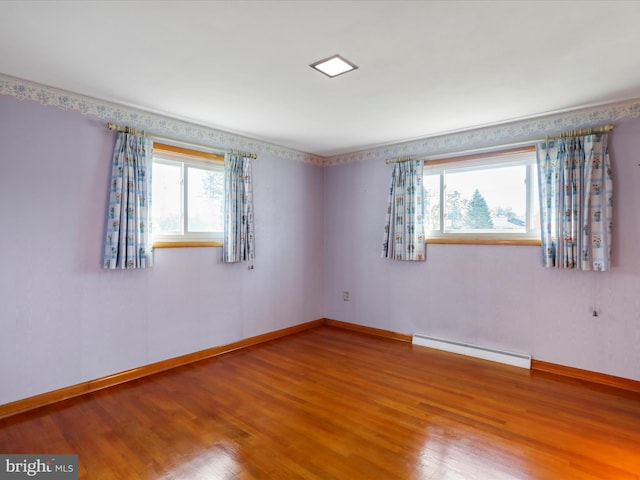 empty room with hardwood / wood-style floors, a baseboard radiator, and plenty of natural light