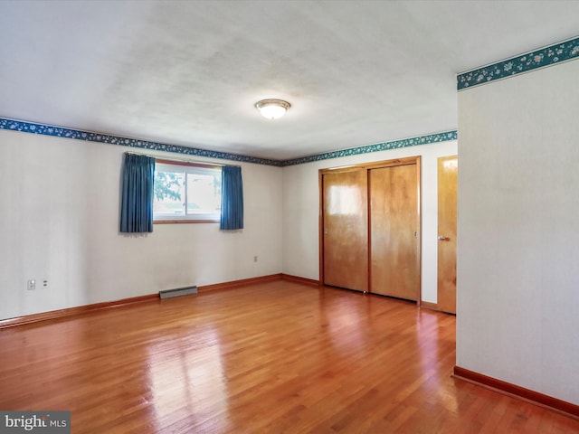 unfurnished bedroom with a baseboard radiator, wood-type flooring, and a closet