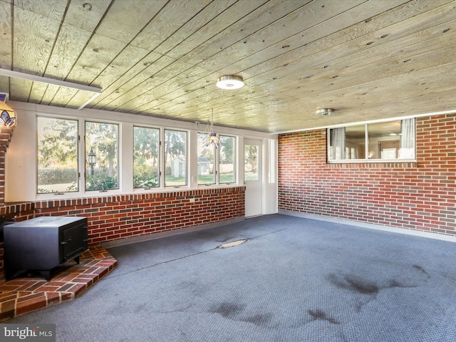 unfurnished sunroom featuring a wood stove, a healthy amount of sunlight, and wooden ceiling