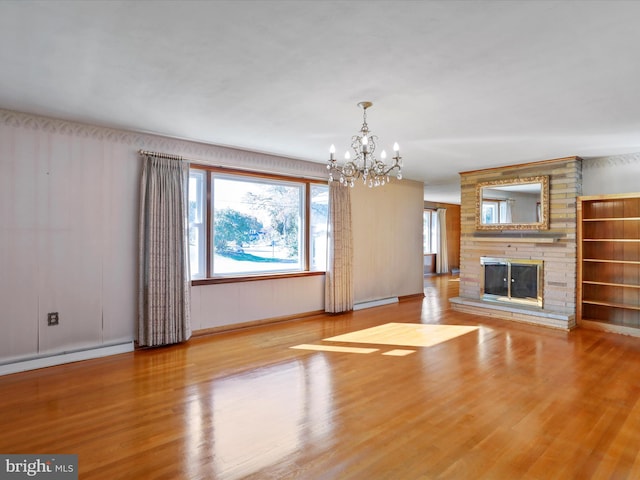 unfurnished living room featuring a baseboard radiator, a notable chandelier, a fireplace, and light hardwood / wood-style floors