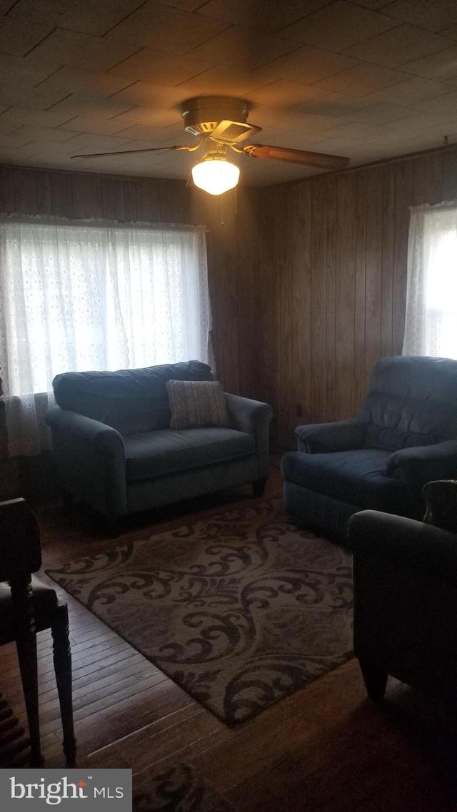 living room featuring wooden walls, ceiling fan, and wood-type flooring