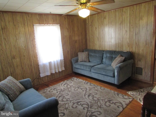 living room with wood walls, hardwood / wood-style floors, and ceiling fan