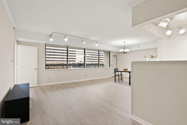 unfurnished living room featuring light hardwood / wood-style flooring, a notable chandelier, crown molding, and rail lighting