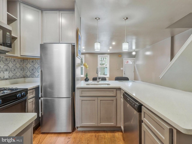 kitchen featuring light hardwood / wood-style flooring, kitchen peninsula, backsplash, sink, and appliances with stainless steel finishes