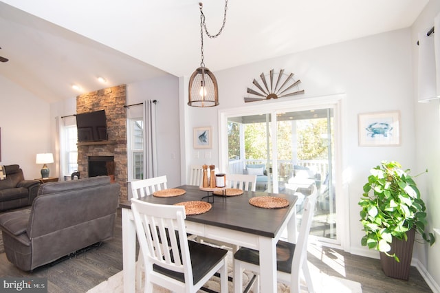 dining room with dark hardwood / wood-style flooring, a stone fireplace, and lofted ceiling