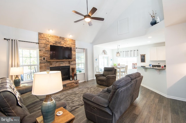 living room with ceiling fan, dark hardwood / wood-style flooring, a stone fireplace, and high vaulted ceiling