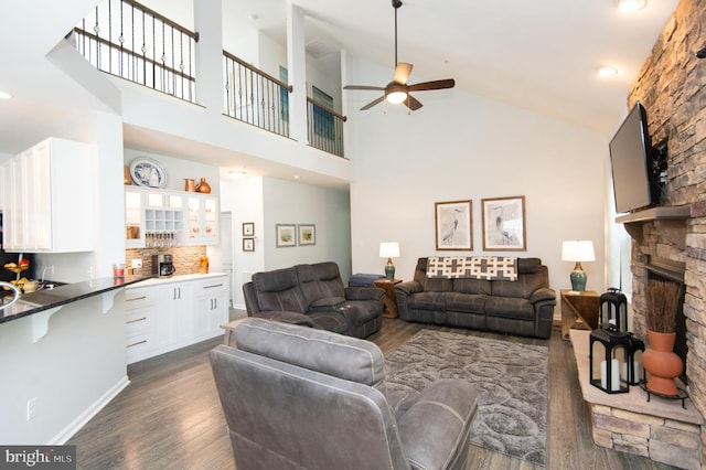 living room with dark hardwood / wood-style flooring, high vaulted ceiling, ceiling fan, and a stone fireplace