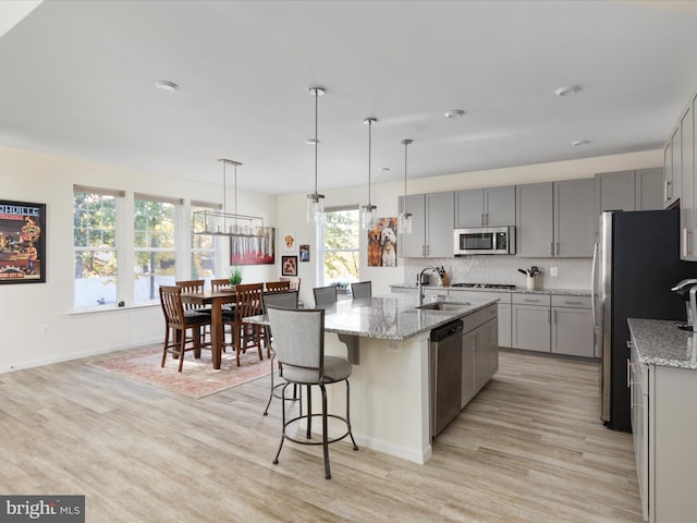 kitchen with a healthy amount of sunlight, light stone counters, stainless steel appliances, and light wood-type flooring