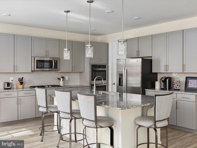 kitchen with a center island with sink, appliances with stainless steel finishes, light wood-type flooring, gray cabinetry, and decorative light fixtures