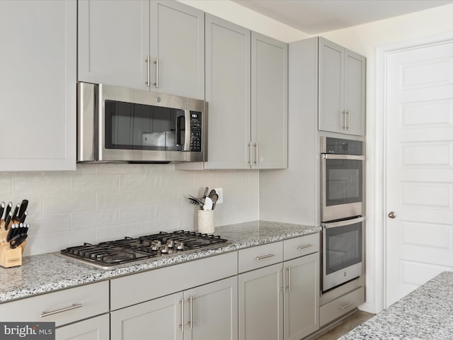 kitchen with gray cabinetry, light stone counters, stainless steel appliances, and decorative backsplash