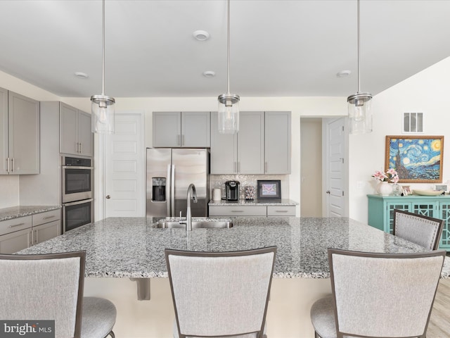 kitchen with stainless steel appliances, sink, pendant lighting, and a kitchen island with sink