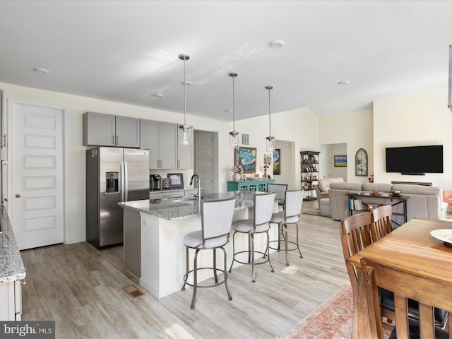 kitchen with gray cabinets, light stone counters, stainless steel refrigerator with ice dispenser, and light hardwood / wood-style floors