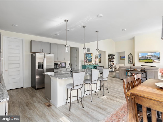 kitchen with gray cabinets, light stone counters, light hardwood / wood-style floors, and stainless steel fridge with ice dispenser