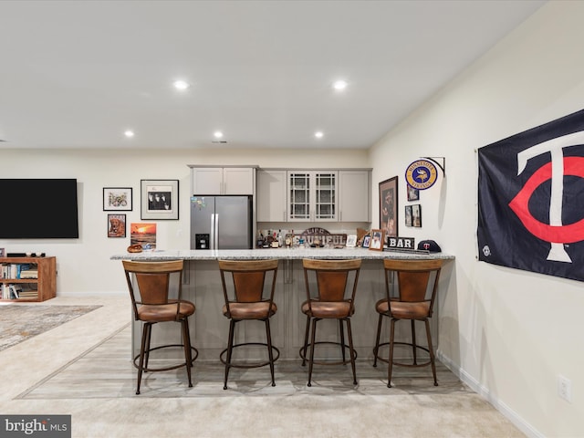 bar featuring stainless steel refrigerator with ice dispenser, light colored carpet, and gray cabinetry