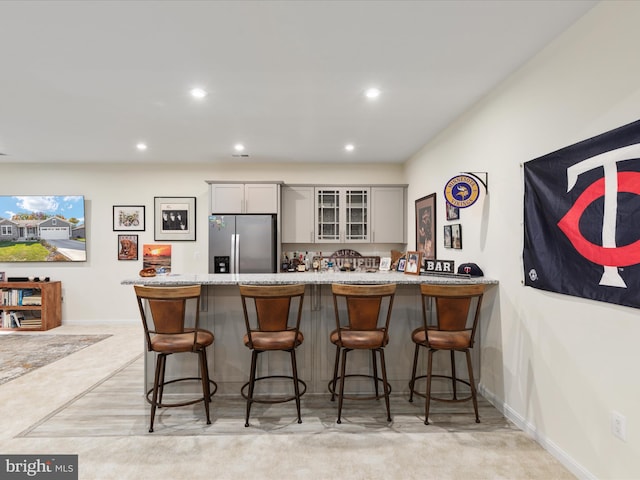 kitchen with gray cabinetry, a kitchen bar, kitchen peninsula, light carpet, and stainless steel fridge with ice dispenser